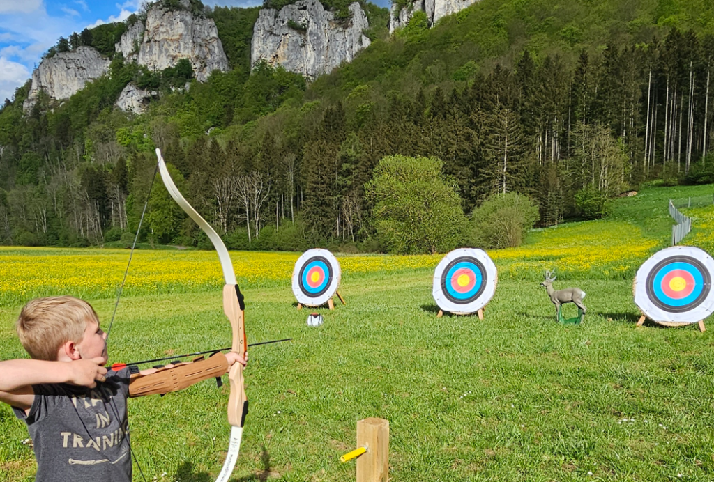 junge schießt mit pfeil und bogen auf eine zielscheibe vor der kulisse der felsen im doanutal